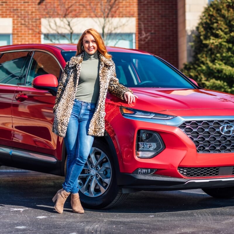 woman in white and black scarf and blue denim jeans standing beside red mercedes benz car